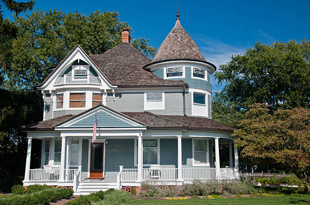 A Victorian style home with wrap-around porch Beautiful gray traditional victorian house.  House has an American Flag haning over the porch and shows a beautiful garden with flowers and trees.  Set against a cloudless blue sky victorian style stock pictures, royalty-free photos & images