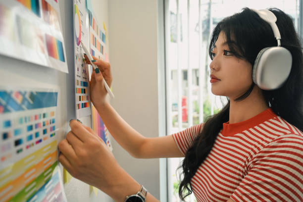 istock Creative woman wearing headphone working with color palette, choosing color samples on whiteboard at graphic studio 1654386225