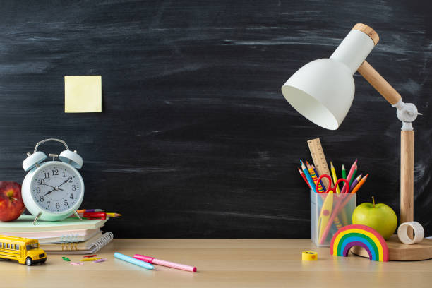 istock Learning materials layout. Side view photo of pencils, ruler, stack of copybooks, plasticine, apples, lamp and more on desk against a chalkboard background. Empty space for text or promotional content 1654408019