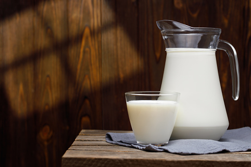 milk in glass and jug on wooden table with sun rays