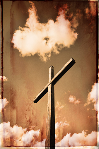 Grungy retro wooden cross among clouds.