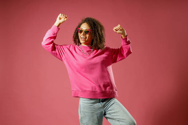 istock Woman in heart-shaped glasses with raised hands looking at side standing on pink studio background 1654481853