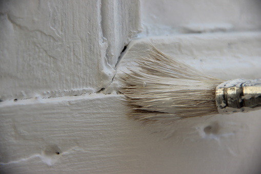brush painting a wooden shutter in white