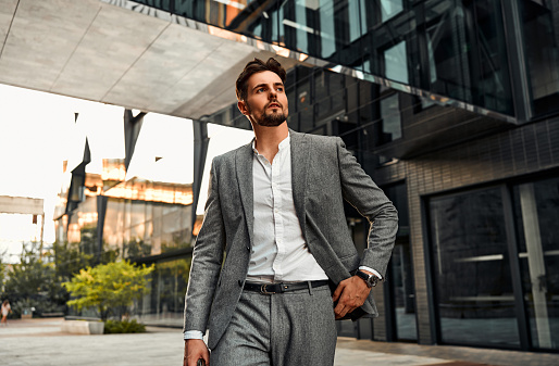 Portrait of attractive confident modern serious stylish man wearing white shirt and gray suit walking outside in business center before work and looking away.