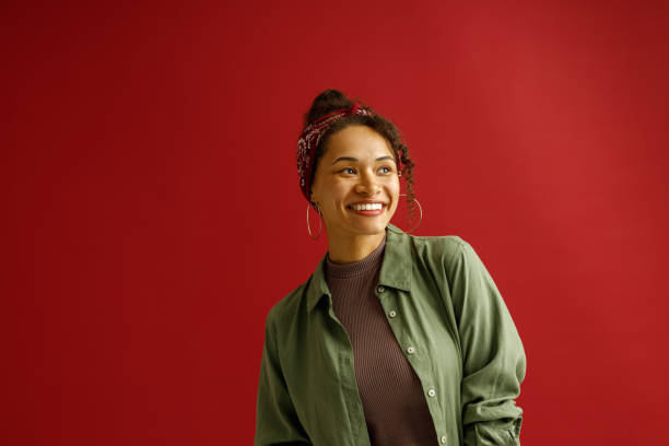 istock Stylish woman looks away with smile while standing on red studio background 1654497946