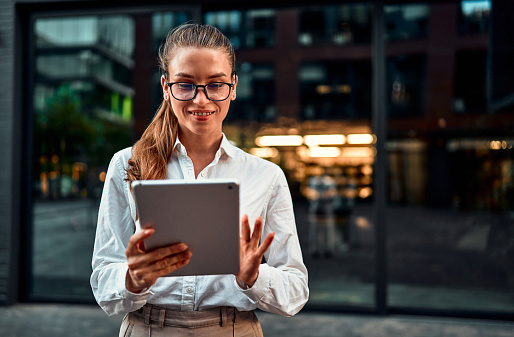 Portrait of beautiful successful confident modern business lady using tablet while standing outside near office. Copy space.Concentrated on work.