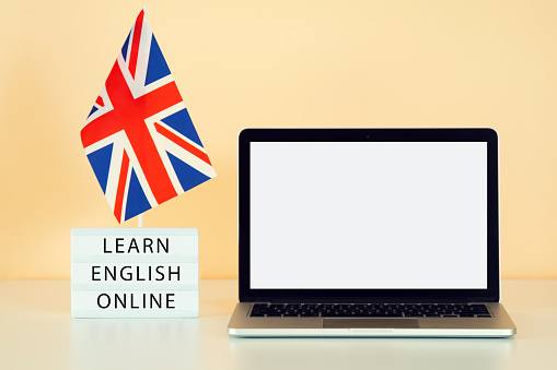 The UK flag next to a laptop with a white screen against orange wall background. Text learn english online. Mockup for banner ad about online English courses.