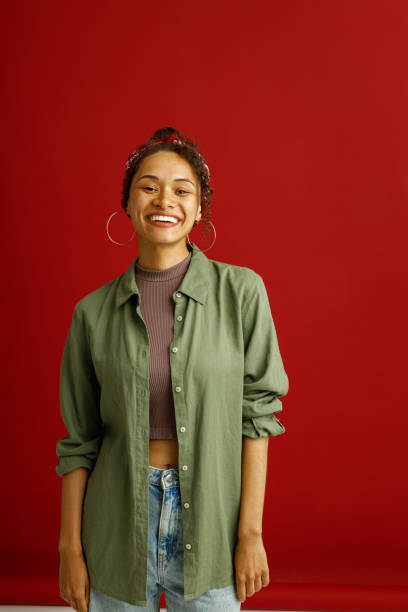 istock Pretty woman looks camera with smile while standing on red studio background 1654524359