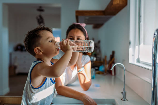 母親と彼女の幼児は、蛇口からすぐにろ過された水でグラスを満たしています - faucet glass water running water ストックフォトと画像