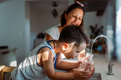 Mother and her toddler filling a glass with filtered water right from the tap