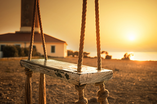 Silhouette of wooden swing with beautiful sunset on the hill near the sea