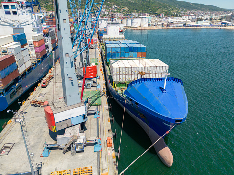 Aerial drone view above sea port. Cargo vessel is loading containers and bulk. Professional business logistics and transportation of cargo ship.