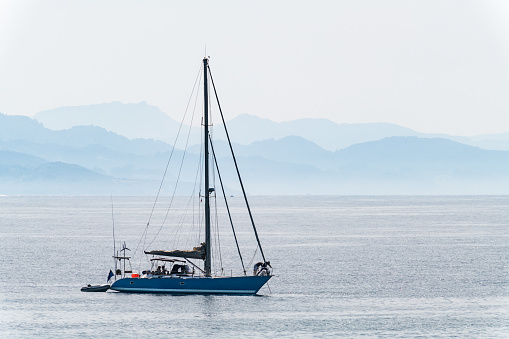 A lonely blue sailboat anchored inside the Ria de Pontevedra in Galicia on a foggy spring day, with the hills of the Southern part of the Ria in the background.
