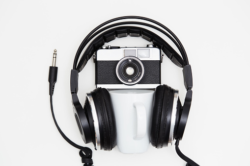 Music and photography but first coffee. SLR film camera and music headphones with a coffee mug on white background