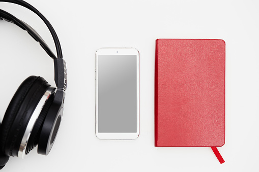 Headphones, smart phone and a red note book on white background