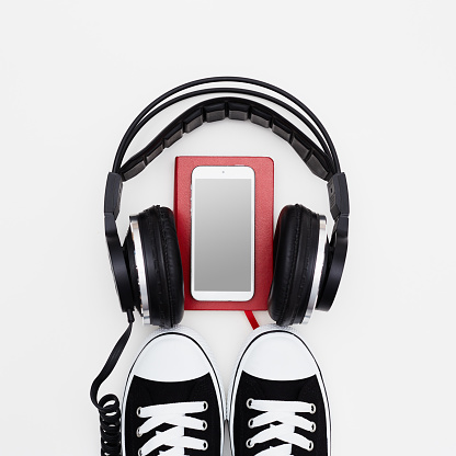 Headphone, smart phone, red book and sneakers on white background