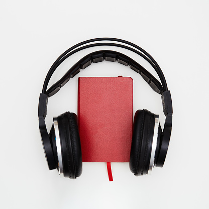 Audiobook. Red book and wireless headphones on white background