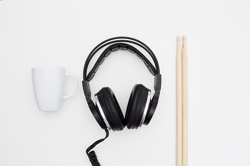 Wired headphones, coffee mug and wooden drumsticks on white background
