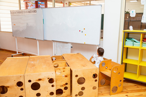 Toddler girl sitting on a wooden bench in the empty school classroom