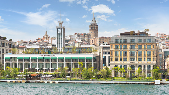 Istanbul, Turkey - May 8 2023: Exterior of Peninsula five stars hotel, suited by Bosphorus Strait, beside Galataport, with Galata tower in the background, in a spring day