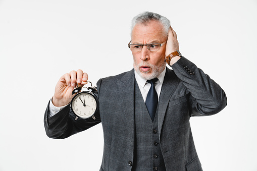 Shocked surprised impressed caucasian middle-aged businessman grandfather lawyer holding clock for deadline, time is out, limited project isolated in white background
