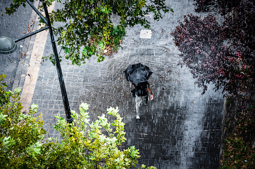 Aerial view of a man with umbrella walking under heavy rain. High resolution 42Mp outdoors digital capture taken with SONY A7rII and Canon EF 70-200mm f/2.8L IS II USM Telephoto Zoom Lens