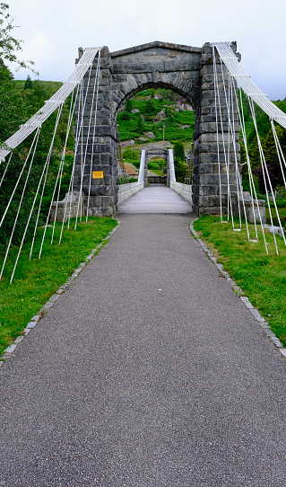 Fort Augustus, Scotland, July 6, 2023. Small suspension bridge over the River Caledonia (Called the Bridge of Oich) near Fort Augustus just off A82 in Scottish highlands. Set in wooded hillside valley. Summer day outdoors