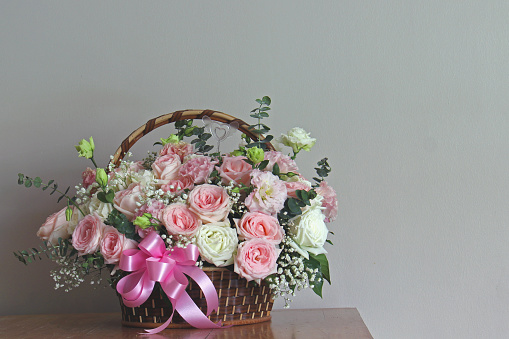 Beautiful colourful blossoming basket of fresh blossoming flowers, close up view. White and pink rose boquete on wooden table