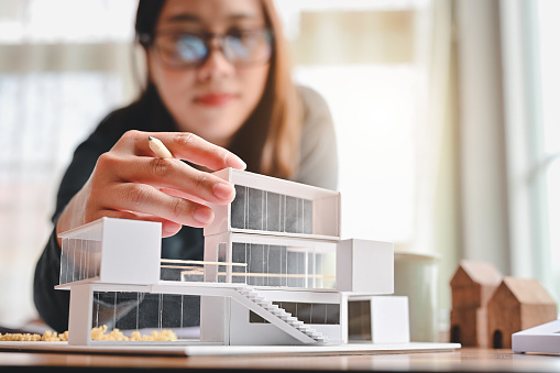 Undergraduate architecture students work on models of the modern box house. Holding the part of the model while thinking about concepts of building and construction. Focusing on her hand.