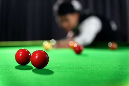 Snooker red ball with snooker player blur in background while aiming red ball on snooker table.