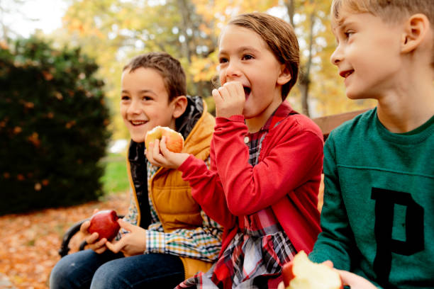 Smiling children eating apples in autumn park