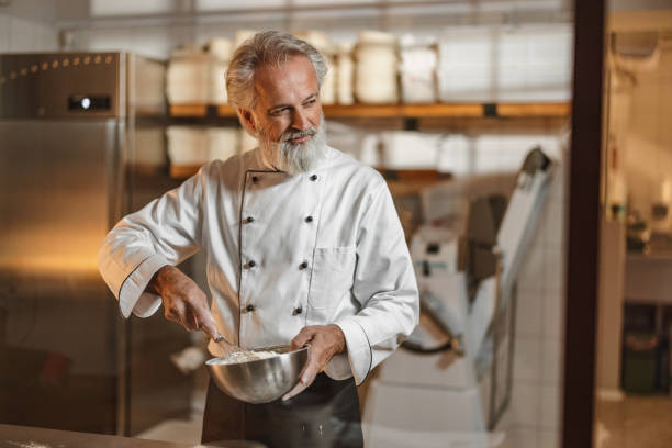 istock Mature Caucasian Baker Holding A Metal Bowl While Mixing A Dough 1654901412