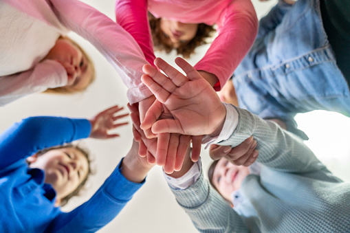 Diverse group of primary age school children all with hands in a huddle playing games - Lifestyles concepts