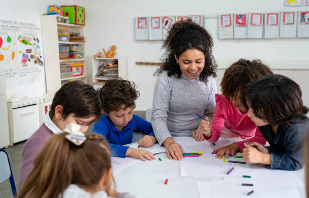 istock Focused school kids coloring with crayons while cheerful teacher supervises 1654909729