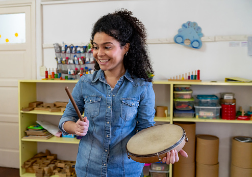 Female happy teacher holding an instrument during music class while facing her students - Education and place of work concepts
