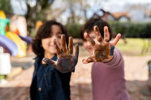 Caucasian 7 year old students showing their hand with fresh paint to camera while playing at the school's playground - Education concepts