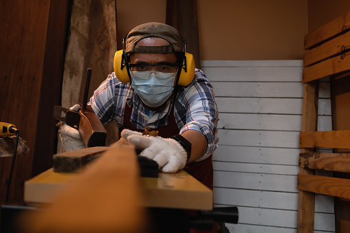 Carpenter working hard while looking level-line plane on wood and planing on wood with a manual wood planer or plane tool in workshop or carpentry workplace, Craftsman, Handyman concept.