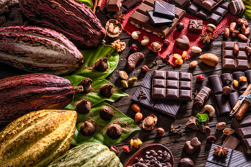 Food theme series: Table top view of a large assortment of chocolate, nuts and dried fruits with cacao fruits on a wooden rustic table