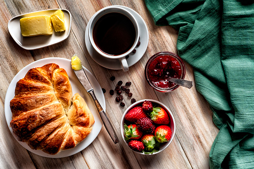 Food theme series: Table top view of breakfast with croissants, marmalade, fruits, coffee cup and butter on wooden table