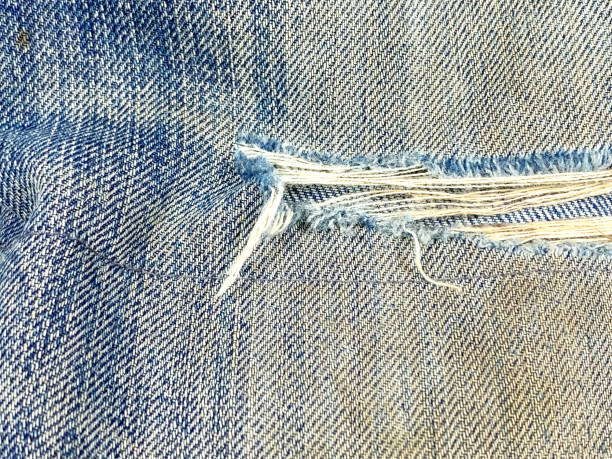 Destroyed torn denim blue jeans texture. Ripped denim blue cloth background. The dirty jeans with holes are torn and rotted so that the threads are visible