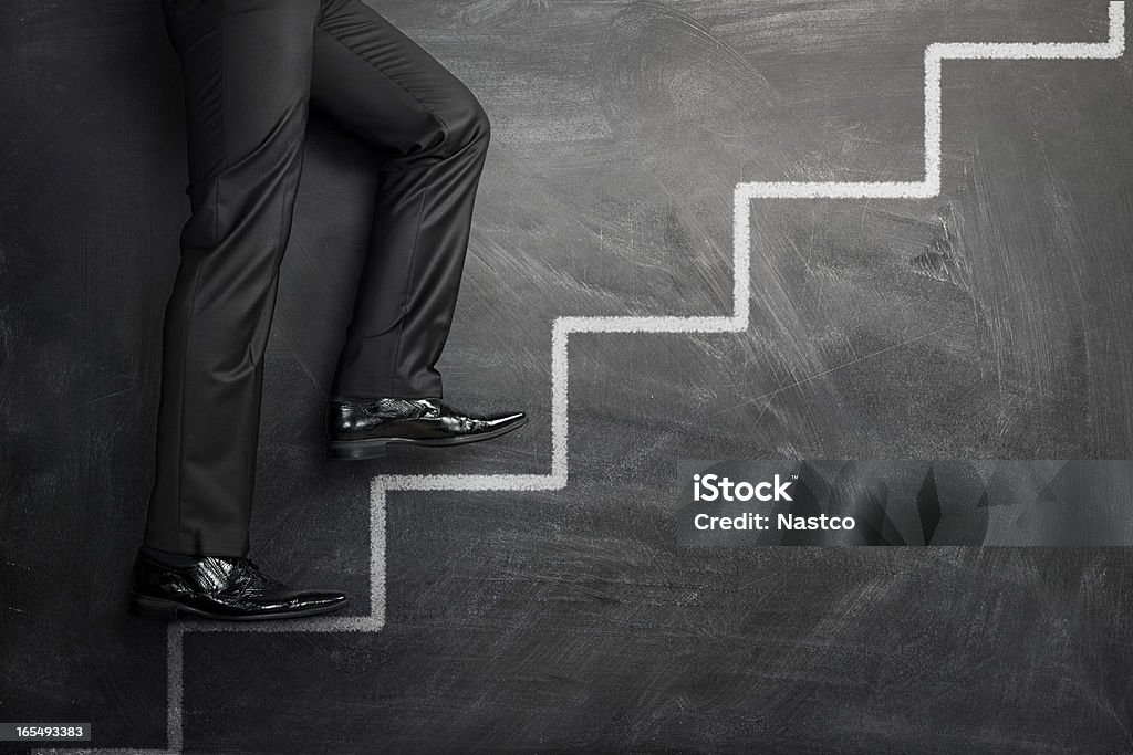 Climbing the career stairs Close up of businessman walking up the career stairs drawn on a black chalkboard with copy space Stepping Stock Photo