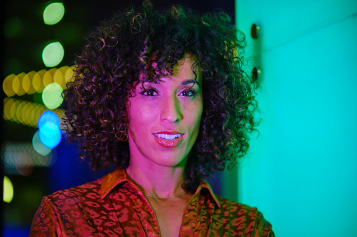 A young woman portrait taken at night in an urban environment with colorful lights.