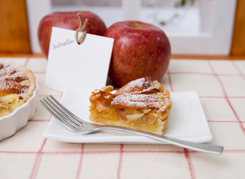 piece of apple tart and red apples, invitation card is placed on the table.