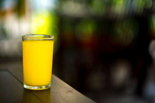 A glass of orange juice on a wooden table is photographed in close-up with a bokeh background.