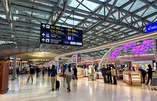 A young backpacker looking looking at departure/arrival screens at an airport. She is wearing a protective face mask to reduce the spread of COVID-19.