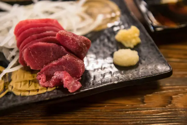 Horsetail meat raw sashimi with wasabi, ginger, soy sauce on dish by wooden table in Japanese restaurant