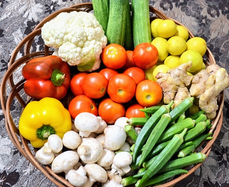 Different types of vegetables in a basket. Fresh and full of nutrients. There are mushrooms, tomatoes, cucumbers, cauliflower, lemons, ginger, ladyfingers, yellow and red bell peppers. Seasonal.