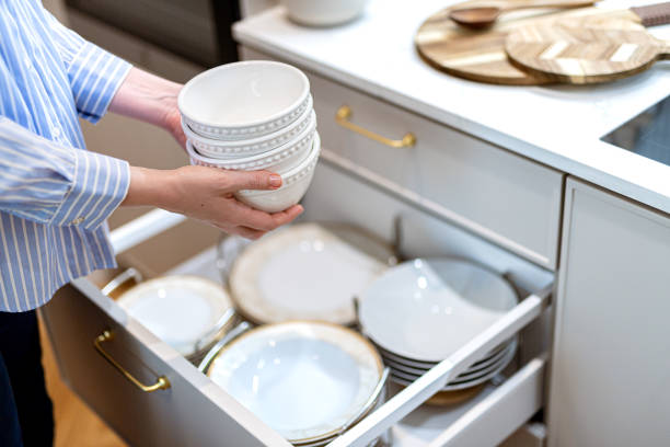 mulher organizando pratos de porcelana e tigelas na gaveta da cozinha. sistema de armazenamento em armários de cozinha - home interior women domestic kitchen cabinet - fotografias e filmes do acervo