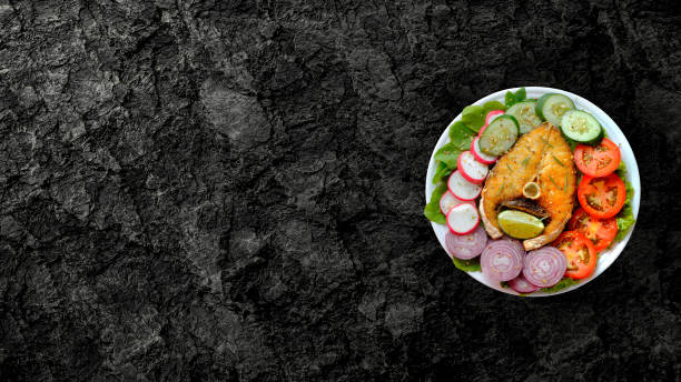 white plate with fish fillet and fresh salad with copy space isolated over rustic dark stone