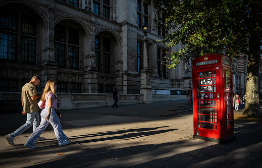 London, UK: People walking on the pavement with the evening sun casting long shadows. Outside the Victoria and Albert Museum in South Kensington, London.